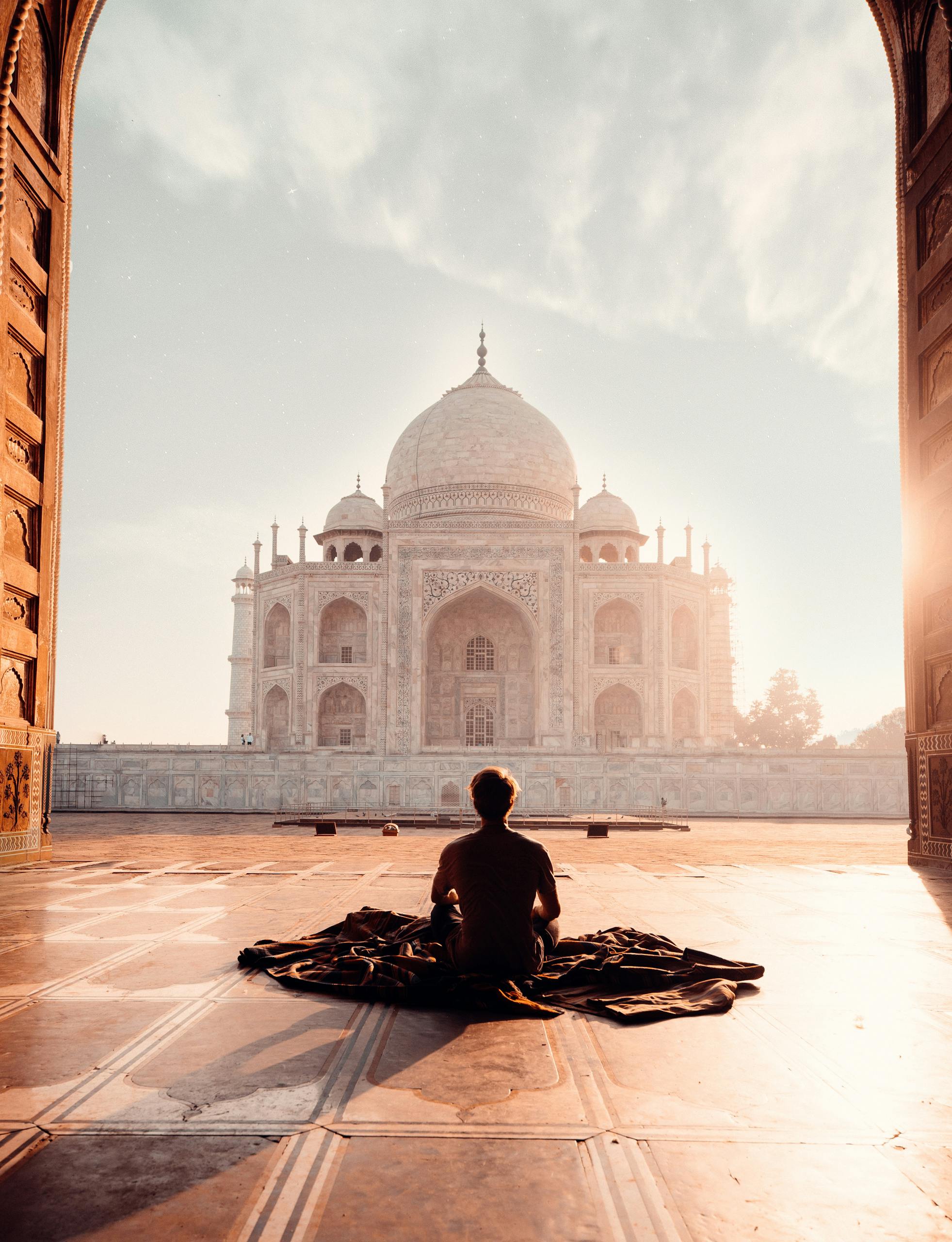 A person meditates at sunrise facing the iconic Taj Mahal, capturing serenity and majesty.