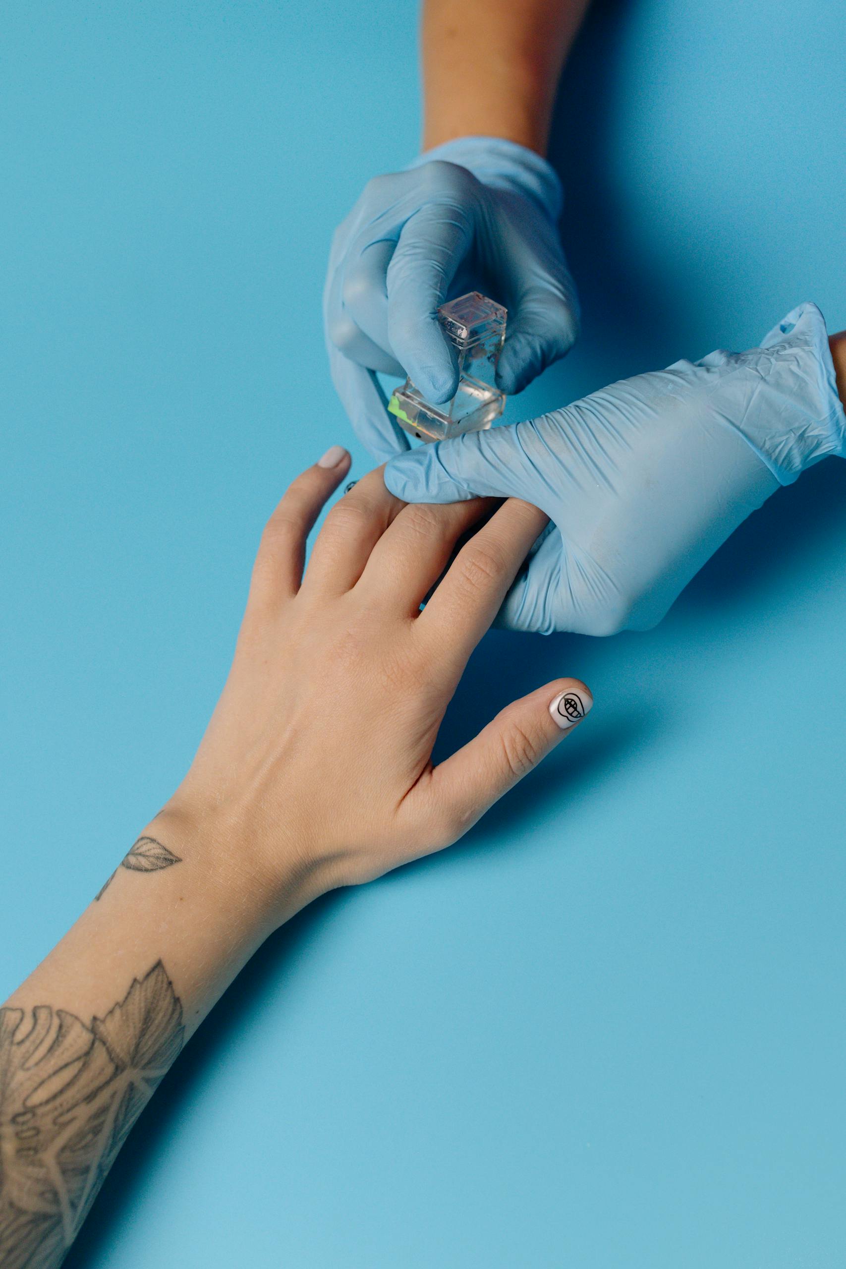 Close-up of a manicure session with latex gloves, nail art, and tattoos against a blue background.